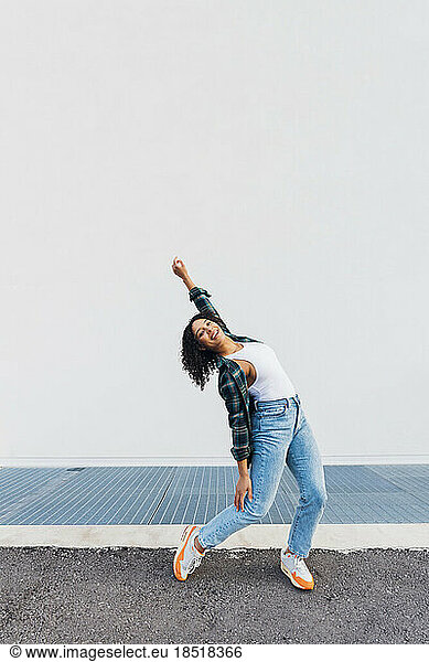 Smiling young woman dancing in front of white wall