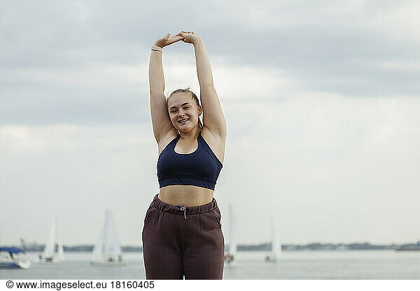 Smiling young woman doing stretching exercise in front of sea