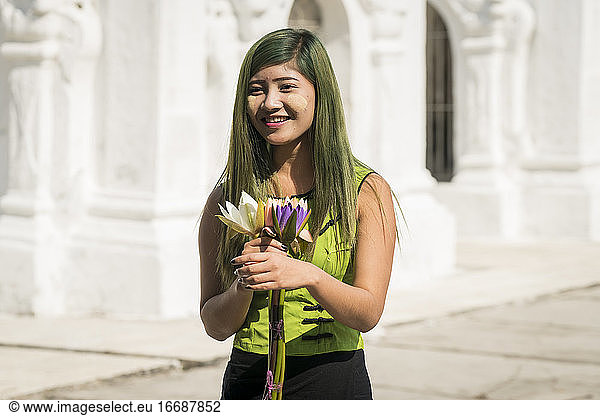 Smiling young woman dressed in green casuals holding flowers in front of Kuthodaw pagoda  Mandalay  Myanmar