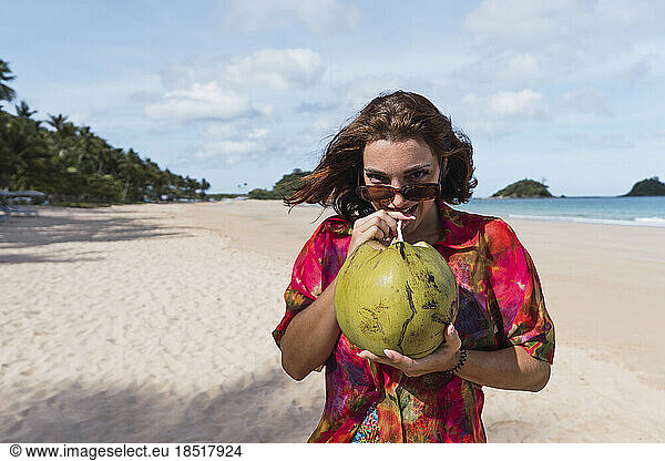 Smiling young woman drinking coconut water at beach