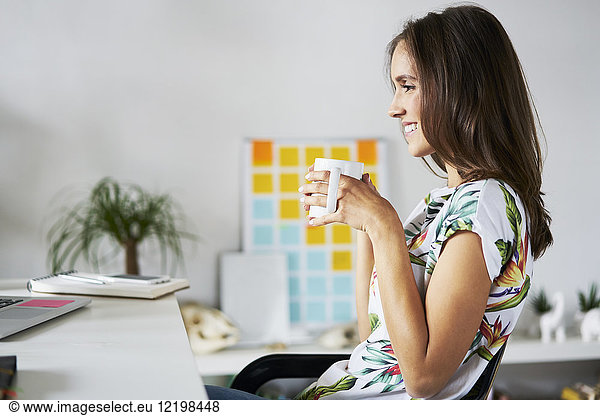 Smiling young woman drinking coffee at desk