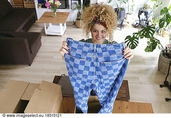 Smiling young woman examining checked jeans at home