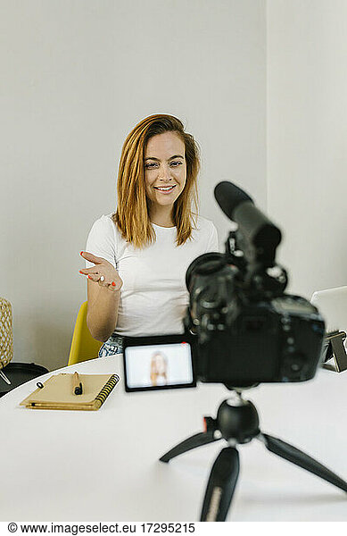 Smiling young woman gesturing while vlogging at home