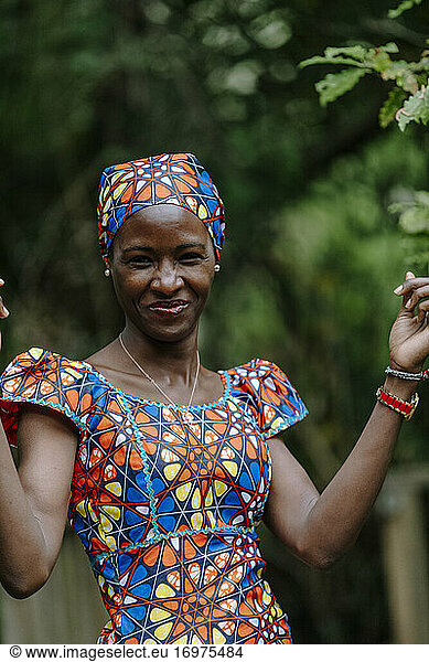 Smiling young woman hands up wearing african dress by garden