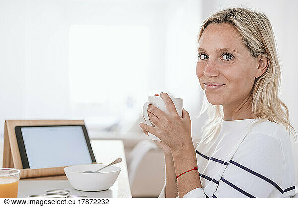 Smiling young woman having coffee at home