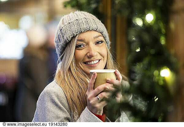 Smiling young woman holding coffee cup at Christmas market