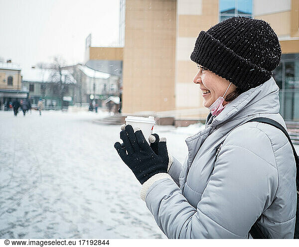 Smiling young woman holding cup on a walk on winter day
