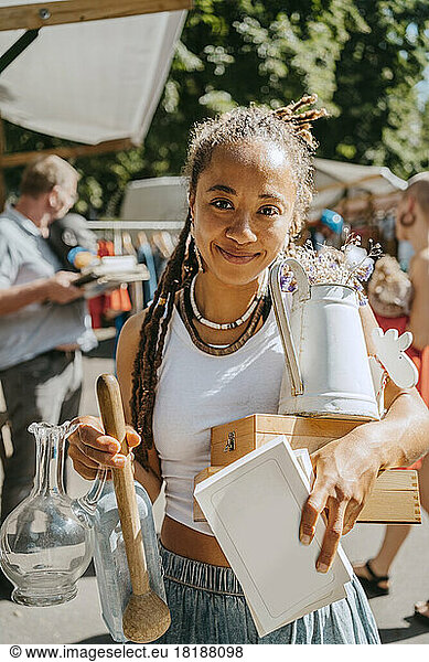Smiling young woman holding different objects while shopping at flea market