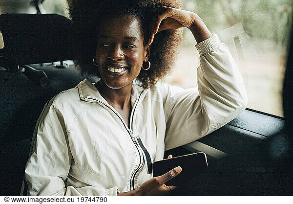 Smiling young woman holding smart phone while leaning on window of van