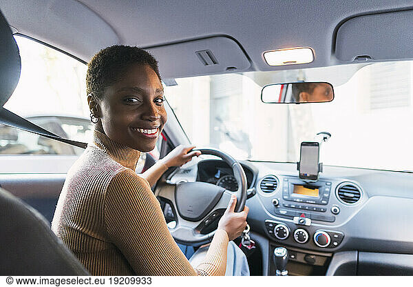 Smiling young woman holding steering wheel in car