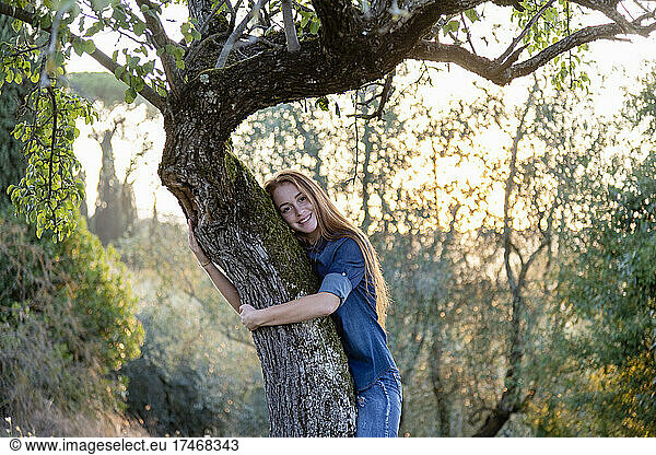 Smiling young woman hugging tree at countryside