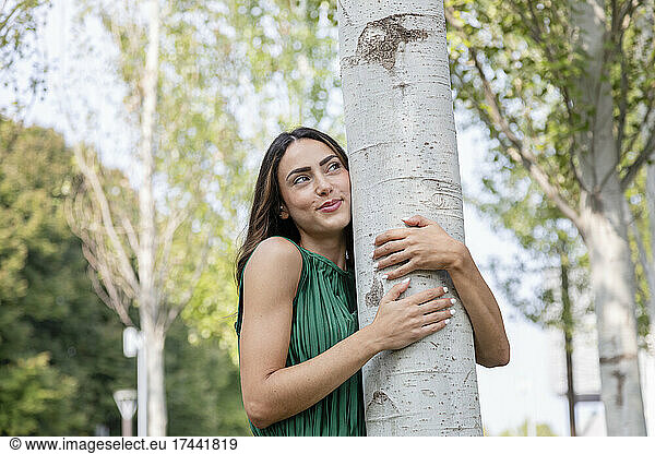 Smiling young woman hugging tree at park