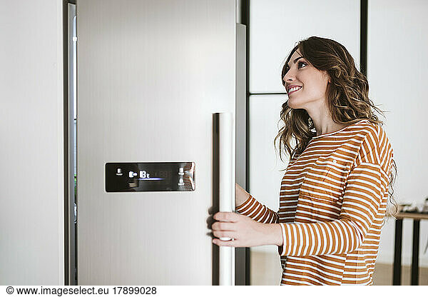 Smiling young woman in kitchen opening fridge