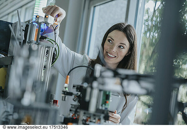 Smiling young woman inventing machinery in laboratory