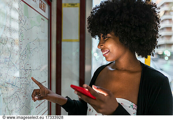 Smiling young woman looking at map while holding smart phone