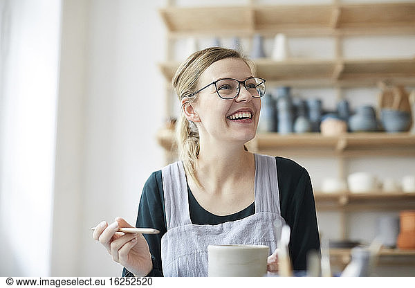 Smiling young woman looking up while learning pottery in art studio
