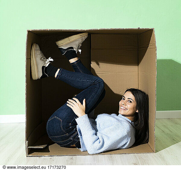 Smiling young woman lying in cardboard against green background