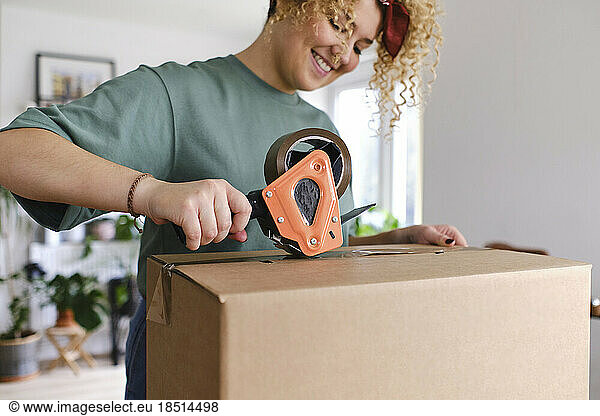 Smiling young woman packing box with adhesive tape