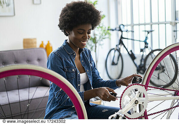 Smiling young woman repairing bicycle at home