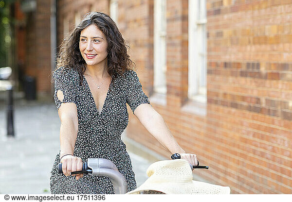 Smiling young woman riding bicycle against building in city