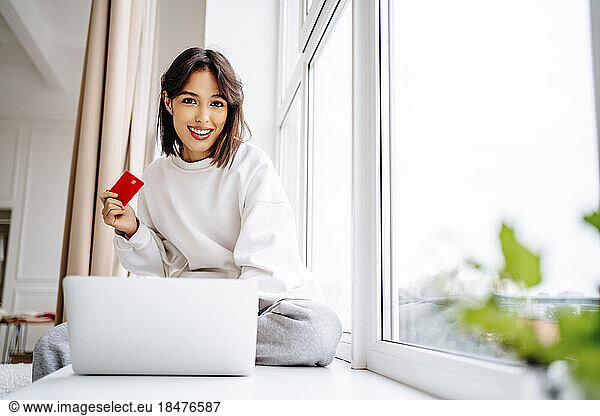 smiling young woman shopping with credit card on laptop at home