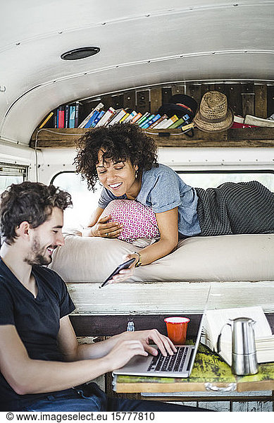 Smiling young woman showing smart phone to man sitting with laptop in motor home