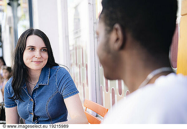 Smiling young woman sitting with man in sidewalk cafe