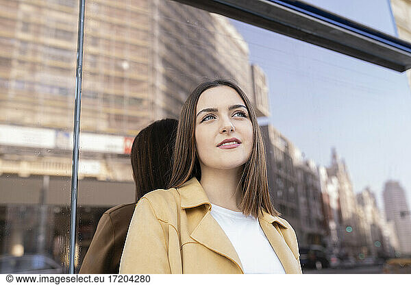 Smiling young woman standing in front of glass wall looking away