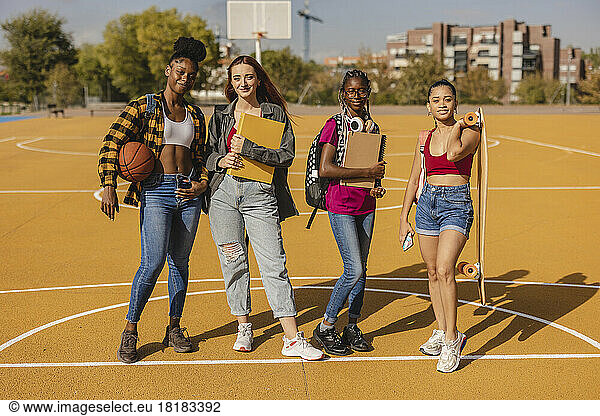 Smiling young woman standing in sports court on sunny day