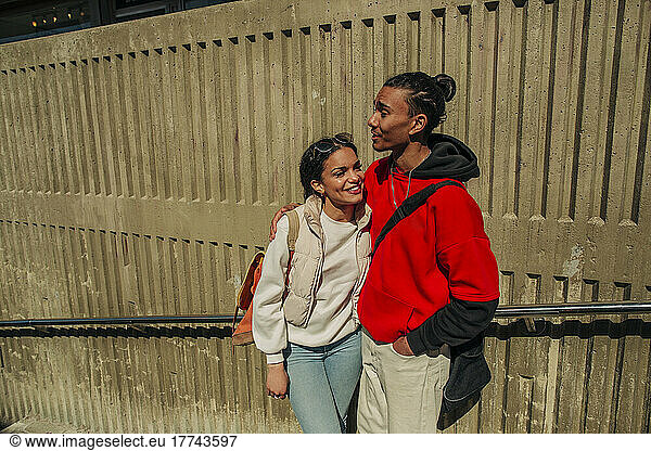 Smiling young woman standing with male friend against wall on sunny day