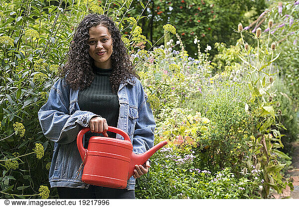 Smiling young woman standing with red watering can
