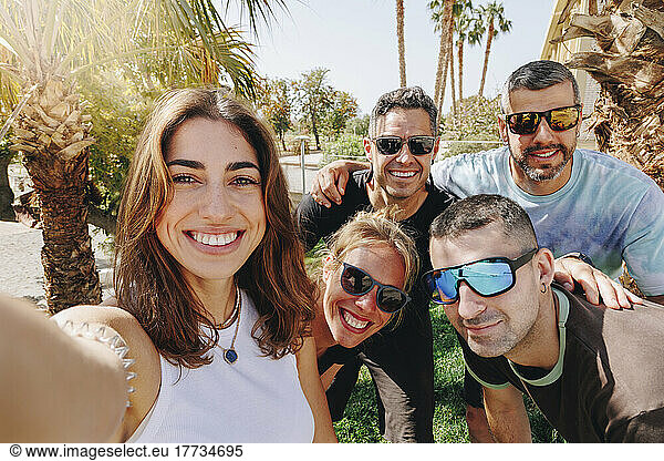 Smiling young woman taking selfie with friends on sunny day