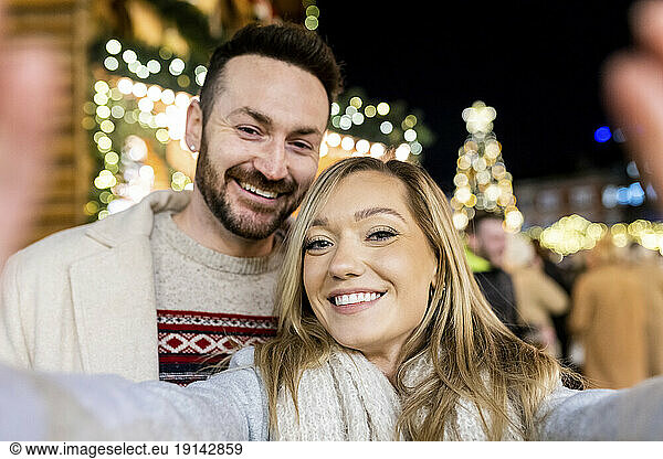 Smiling young woman taking selfie with man at Christmas market
