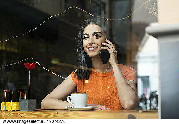 Smiling young woman talking on smart phone sitting in cafe