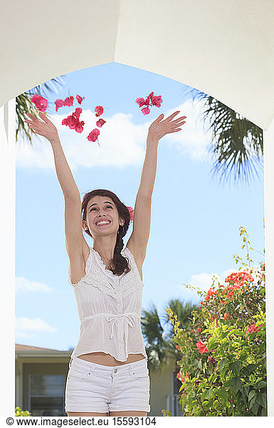 Smiling young woman throwing flower petals in the air