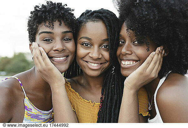 Smiling young woman touching cheeks of female friends