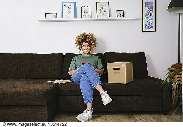 Smiling young woman using smart phone on sofa at home