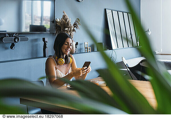 Smiling young woman using smart phone sitting at table