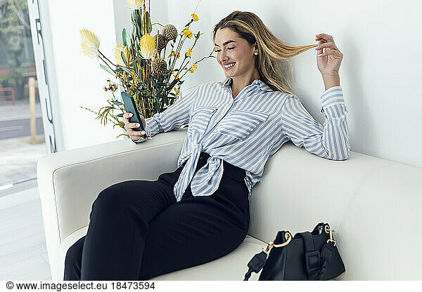 Smiling young woman using smart phone sitting on sofa