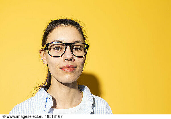 Smiling young woman wearing eyeglasses against yellow background