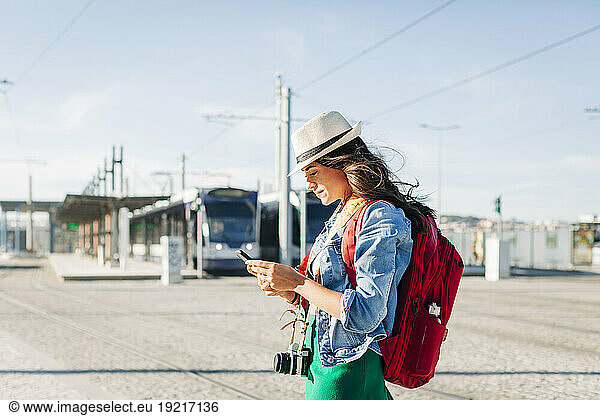 Smiling young woman wearing hat using smart phone on sunny day