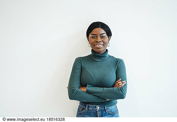 Smiling young woman with arms crossed standing in front of wall