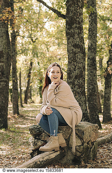 Smiling young woman with brown hair sitting in a forest in autumn