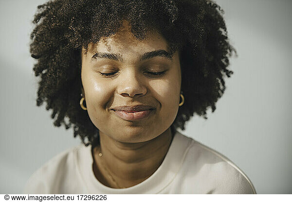 Smiling young woman with eyes closed against white wall