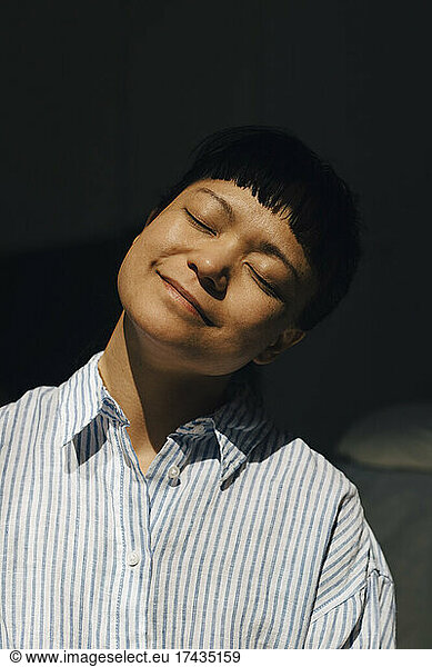 Smiling young woman with eyes closed in sunlight