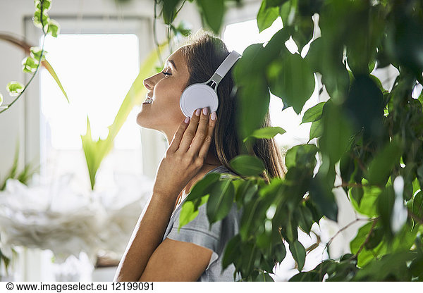 Smiling young woman with headphones listening to music at indoor plant