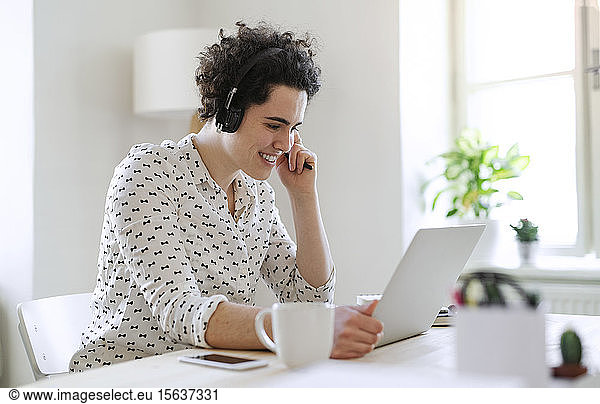Smiling young woman with headset and laptop working at desk