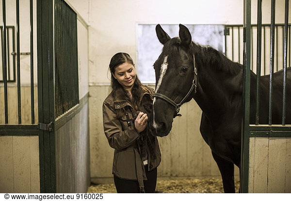 Smiling young woman with horse in stable
