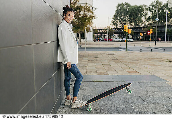 Smiling young woman with skateboard on footpath