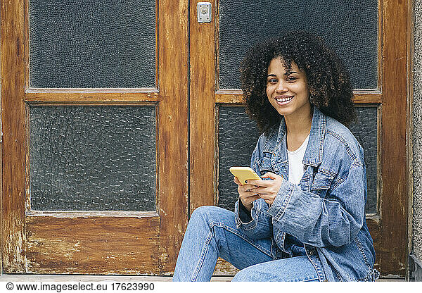 Smiling young woman with smart phone by door